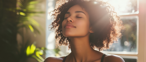 A young woman with curly hair basks in sunlight, eyes closed and serene.