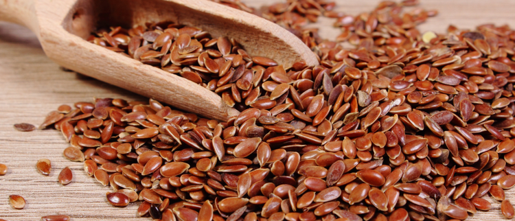 Blog of Flaxseed Oil Benefits: Why This Plant-Based Oil Is a Nutritional Powerhouse which have image A close-up of glossy brown flax seeds spilling from a rustic wooden scoop onto a wooden surface. 