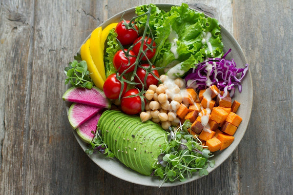 A bowl of fresh vegetables, chickpeas, and avocado arranged on a wooden surface.