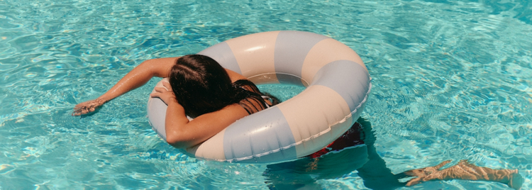 A person floats in a swimming pool on a pastel-striped inflatable ring, resting their head on the side.