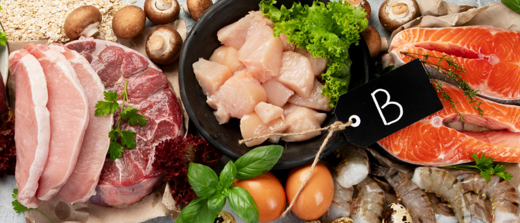 Blog of B-Complex vs B-12: Understanding the Difference which have image A variety of vitamin B-rich foods including raw salmon steaks, chicken breast pieces in a black bowl, pork and beef cuts, shrimp, eggs, mushrooms, oats, and fresh herbs such as basil and parsley, arranged on a rustic surface with a black tag labeled 